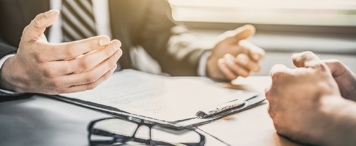 two professionals discussing paper work at a table with a clipboard and glasses on the table commercial litigation