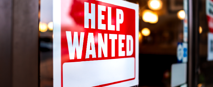 red and white help wanted sign on a store front window employment law